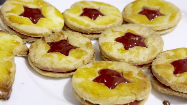 Close-up of homemade Alsatian bredele sandwich cookies with star-shaped red jam filling, golden egg-wash glaze on white plate, festive Christmas holiday dessert