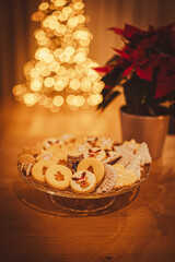 Christmas cookies close up. Christmas cookies on a glass tray. In background Christmas tree. Christmas lights. In the foreground is a red Christmas rose.