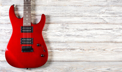 Obraz premium Red electric guitar resting against light wooden background