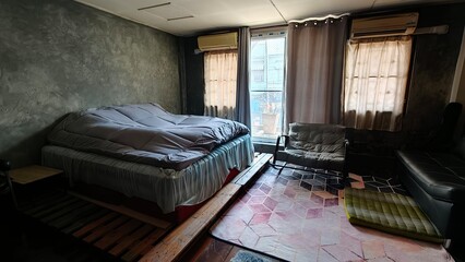 Simple and cozy bedroom interior with a low bed, soft bedding, and minimal furniture. Natural light coming through the window creates a calm and lived-in atmosphere. Suitable for concepts such as home