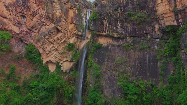 Towering Cato&aacute; Waterfall in Campo Alegre, Tocantins, showcasing its slender emerald cascade against the ancient, multi-toned quartzite cliffs of the Serras Gerais, drone descent, Brazil.