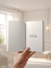 Hand holding open book with year 2026 in bright room for future planning concept