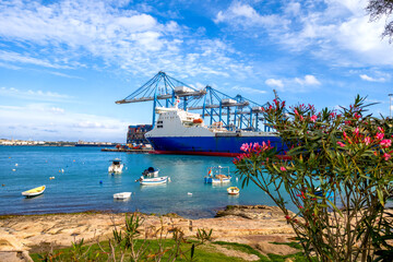 Birzebbuga, Malta &ndash; harbor panorama with cranes, ship hull, small fishing boats in the foreground and detailed industrial atmosphere