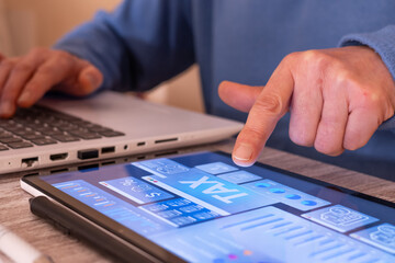 Person using a laptop and a tablet with a digital tax planning dashboard, analyzing financial data and statistics for online payment or accounting purposes