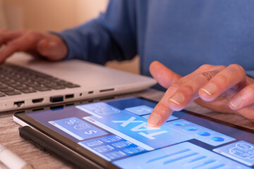 Person's hand interacting with a digital tablet displaying a tax planning dashboard and financial data, while also using a laptop, illustrating technology integration in finance and taxation