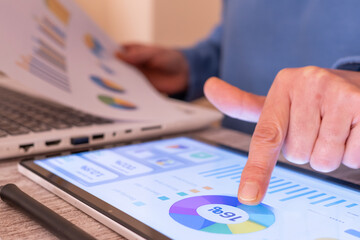 Person reviewing financial charts and calculating taxes on a tablet dashboard while holding printed reports, illustrating modern finance technology, online payments, accounting and budgeting tools