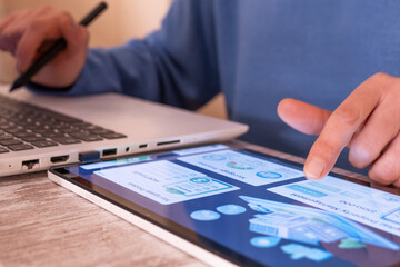 Person using a digital tablet with real estate application interface and a laptop, navigating through property listings, mortgage information, and approval services online