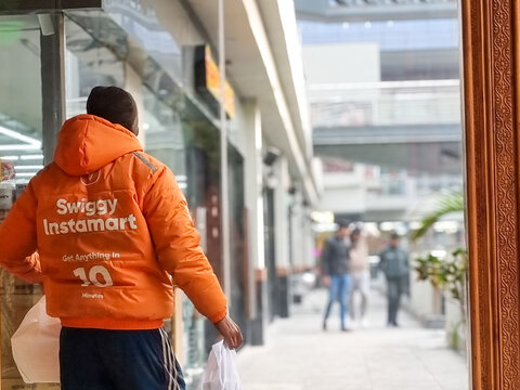 Delivery rider boy agent of hyperlocal quick commerce delivery app Swiggy instamart with 10 min delivery services in heavy jacket delivering during the harsh winters