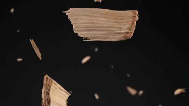 Wood chip fragments floating against dark background conveying motion and closeup texture, dramatic macro splinter and bark detail with airborne debris and warm lighting, cinematic shallow depth