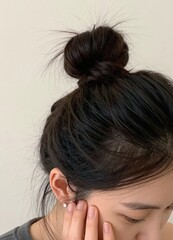Fototapeta premium a close-up view of a woman with their dark hair styled in a bun, with their hand near their face, focusing on the hair details.