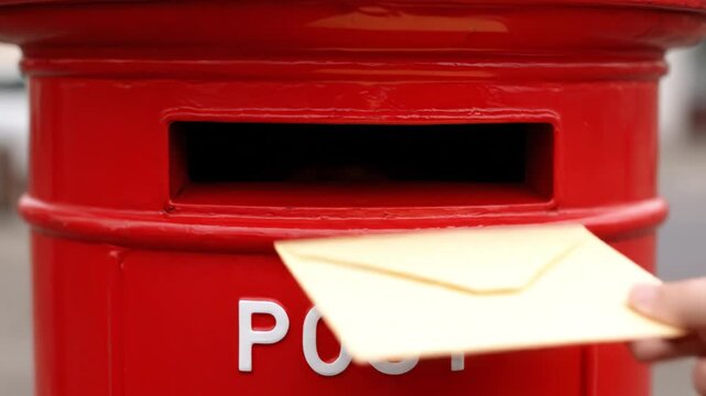 Red postbox letter mail slot posting envelope hand post office delivery concept postal service communication urban outdoor red postbox slot envelope mailing letter being inserted by hand with shallow