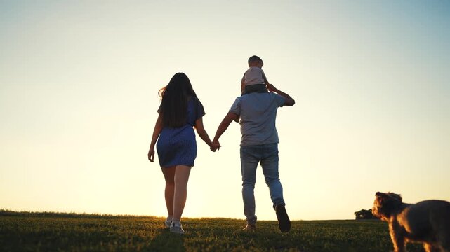 Young couple walking with dog. Silhouette of family walking dog in a park. A mother and dad walking their dogs in nature. A young pair lifestyle strolling with a dog.