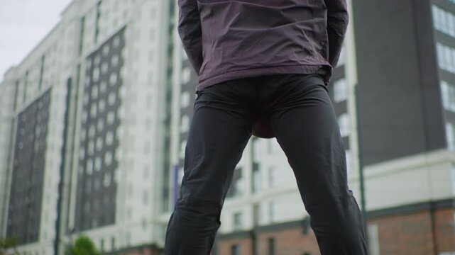 person purple jacket squatting apartment building lowangle urban shot showing bent legs and puffy parka with beanie, concrete pavement and modern highrise background, gritty focused mood conveying