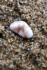 Close-up of a smooth white sea pebble lying on a textured sandy beach. Natural minimalist background inspired by calmness, balance and mindfulness. Concept of nature detail, slow living, meditation an