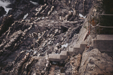 A set of concrete stairs winds down a steep rocky shoreline. The steps are surrounded by a railing and lead towards the ocean. Waves crash against the rocks below