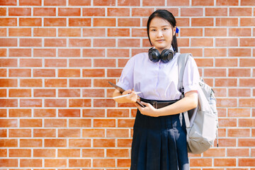 portrait asian teen girl ,highschool student in uniform on school campus brick wall happy smiling