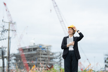 Asian female engineer managing an industrial construction project for a global company, coordinating machinery and safety systems to strengthen business performance and industrial reliability.