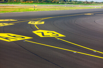 Yellow painted hold position markings and taxiway designations on dark asphalt at an airfield. Aeronautical paint and the dark, textured runway pavement