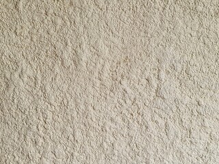 A flat-lay macro shot of a rough, sandy-textured wall surface in a warm beige or light tan tone