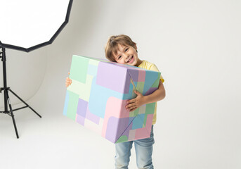 Naklejka premium Young boy smiles holding wrapped gift box indoors.