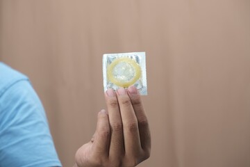 Close-up of hand holding packaged condom, representing safe sex, protection, sexual health awareness, and contraception concepts for education and advertising.