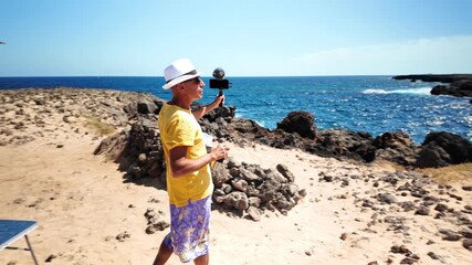 Middle-aged digital nomad creating social media content on a rocky coastline, showcasing a freelancing lifestyle while traveling in a van and working remotely from a beautiful, sunny beach