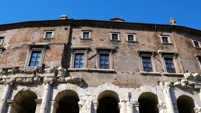 roman structure weathered stone arches ionic columns supporting rustic brick walls tall modern windows beneath bright blue sky upward view rome empire 