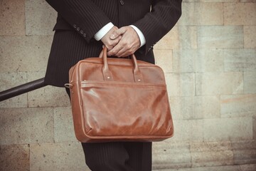 Elegant man in a stylish coat and suit holding a premium leather briefcase. Conceptual photography...