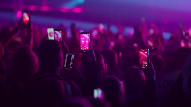 Slow motion crowd jumping dancing and filming live concert as bright stage lights flicker and amplify collective energy
