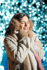 Young woman enjoying the winter season with snow on her face and festive lights behind her