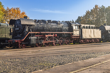 Side view of a massive vintage black steam locomotive of the Veluwsche Stoomtrein Maatschappij parked on tracks during a sunny autumn day.