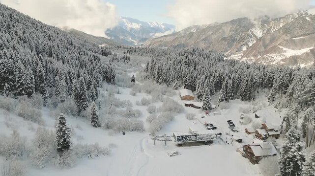 Aerial static snow covered pine forest and wooden hut near ski resort in Mestia, Georgia. Snowy alpine valley landscape, peaceful wilderness. Panoramic Caucasus mountains landscape ad copy background