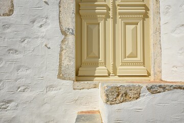 Old Neoclassical house facade with a handcrafted whitewashed stone wall and an elegant wooden entrance door in Astypalaia island, Dodecanese Greece,