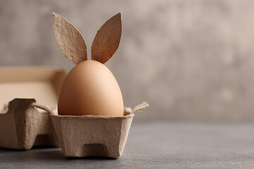 Easter bunny egg in carton with brown ears on a grey background