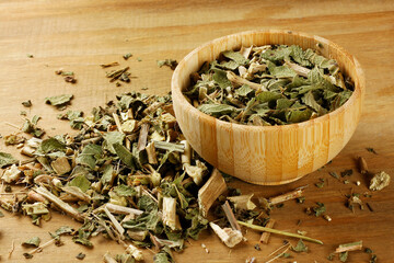 Lemon balm, Melissa officinalis, dried leaves in a wooden bowl, spread out on a rustic wooden table