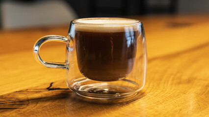 Espresso macchiato in a glass cup staying on a wooden table