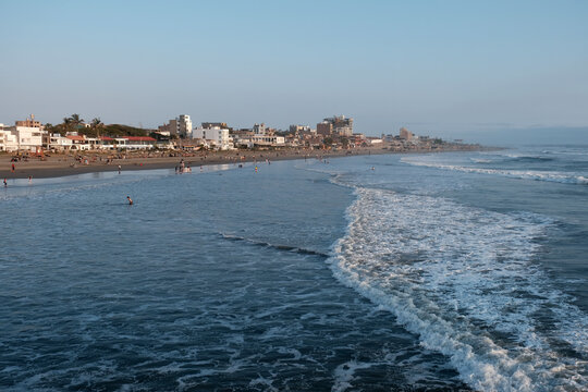 People relaxing and swimming on pimentel beach, peru, with waves rolling to the shore and coastal buildings along the beachfront