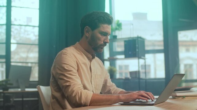 Businessman concentrating on work by window, Individual diligently working with laptop and organized materials