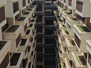 A high-angle, symmetrical perspective looking down the internal atrium of a modern apartment building, featuring rows of identical white balconies with brown privacy screens and built-in planter boxes