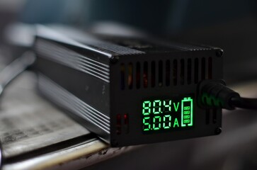 A high-detail macro shot of a digital LCD screen on an electric vehicle battery charger, displaying real-time data including a voltage of 80.4V and a charging current of 5.00A against a dark interface