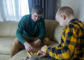 Father teaching his young son to play checkers at home. Warm family moment, parenting, learning through play, quality time together, casual indoor lifestyle scene.