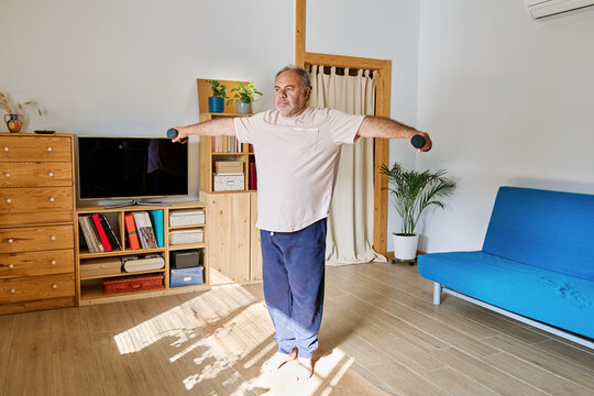 Mature man making exercise with dumbbells at home. Healthy lifestyle for wellness.