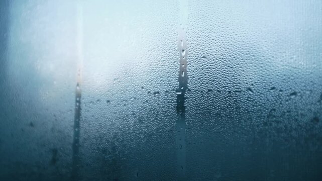 Closeup slow motion video of water drops on glass window. Abstract blue bubbles background. Sad mood on a rainy day.