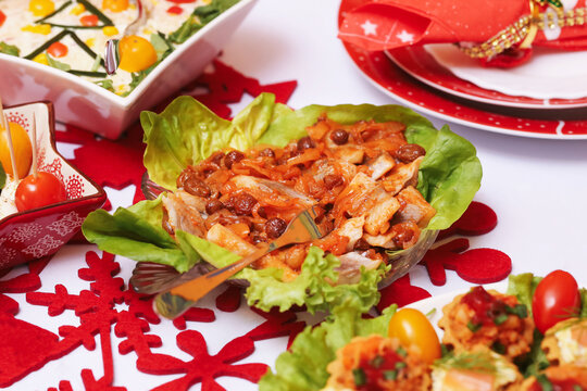 Herring in sweet sour tomato sauce served on lettuce leaves. Traditional Polish Christmas dish. Festive table setting with red decorations. Holiday homemade food closeup. Seasonal family dinner scene.