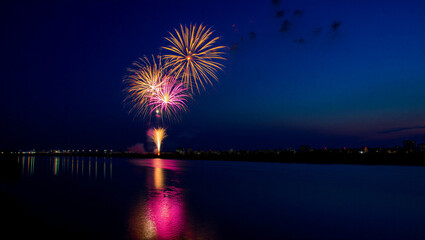 A beautiful colorful firework display explodes in the night sky over the river with a bright reflection on the water during a festive New Year celebration event