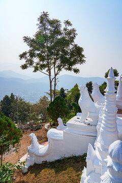White statue of a chinthe overlooking the misty valley of the Wat Phra That Doi Kongmu hilltop temple in Mae Hong Son, Northern Thailand