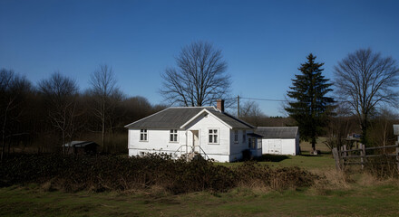 Charming white wooden house nestled amidst bare trees and grassy fields under a clear blue sky, evoking peaceful rural living.