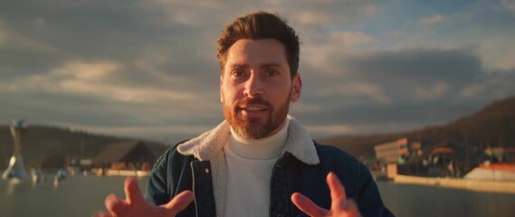 Presenter shares message by harbor, Sunset backdrop highlights speaker with hopeful stance and gestures