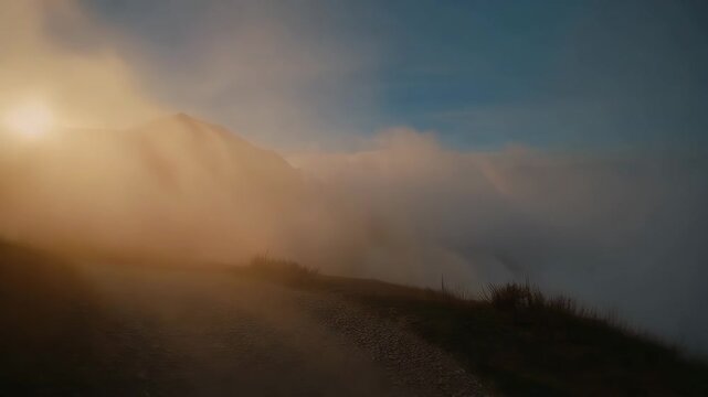 Mountain road disappearing into clouds with rising sun, showing the journey through mist to light