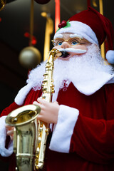 Vertical shot of  toy Santa Claus playing a trumpet surrounded by festive lights and Christmass balls